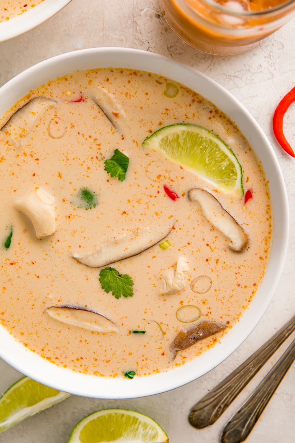 Crockpot Tom Kha Gai soup in a white bowl on a table next to lime wedges.