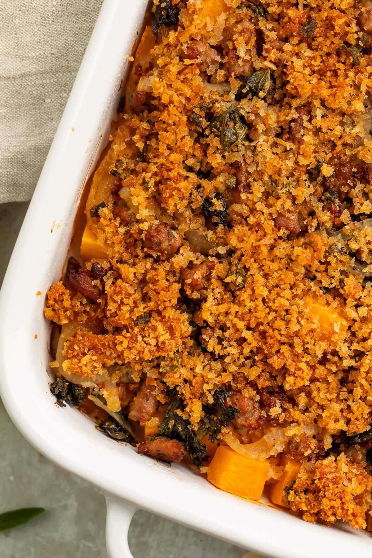 Overhead view of a large white casserole dish, angled on a table, holding a butternut squash casserole topped with breadcrumbs.