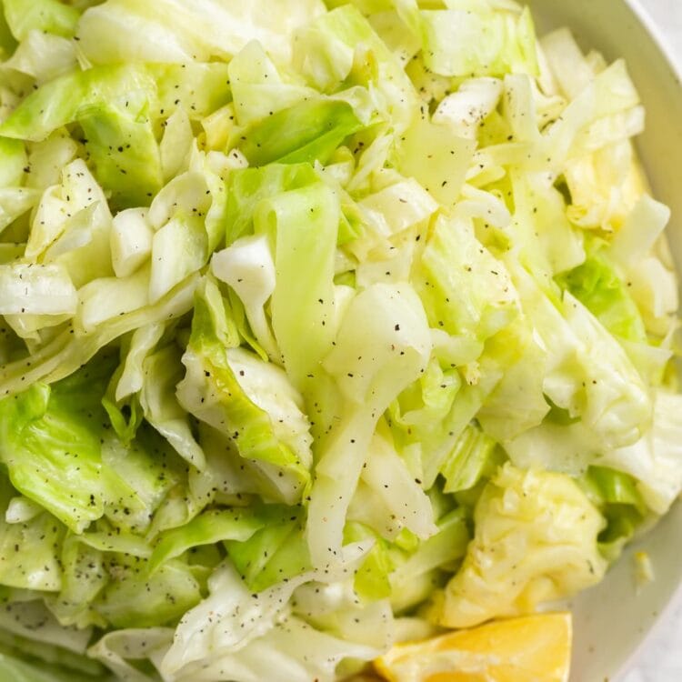 sauteed cabbage in a bowl with fresh lemon sliced and black pepper on the side
