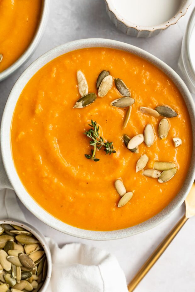 overhead image of sweet potato soup in a bowl with pumpkin seeds and fresh thyme on top