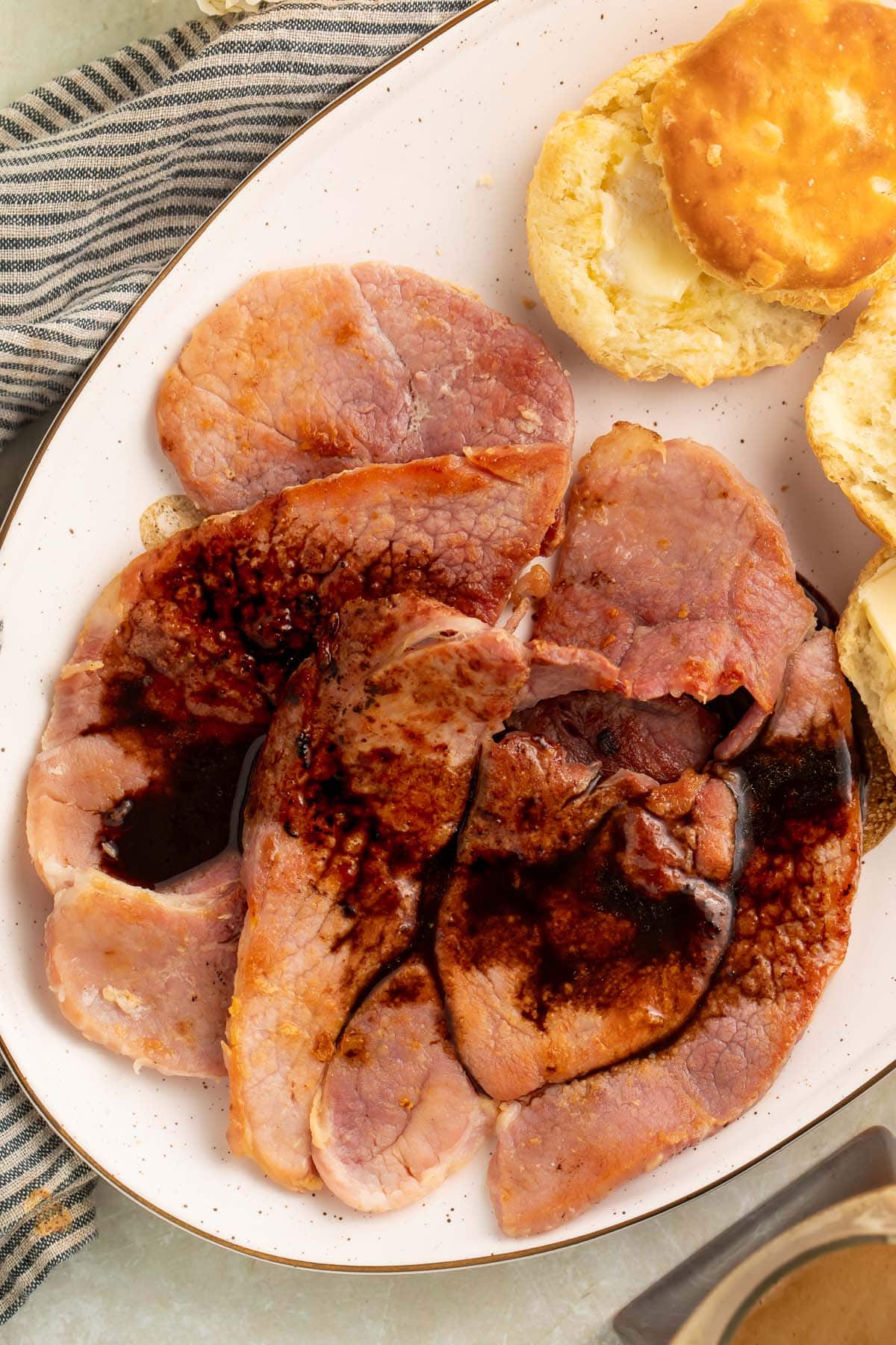 Red eye gravy poured over country ham on an oval platter with fluffy biscuits.