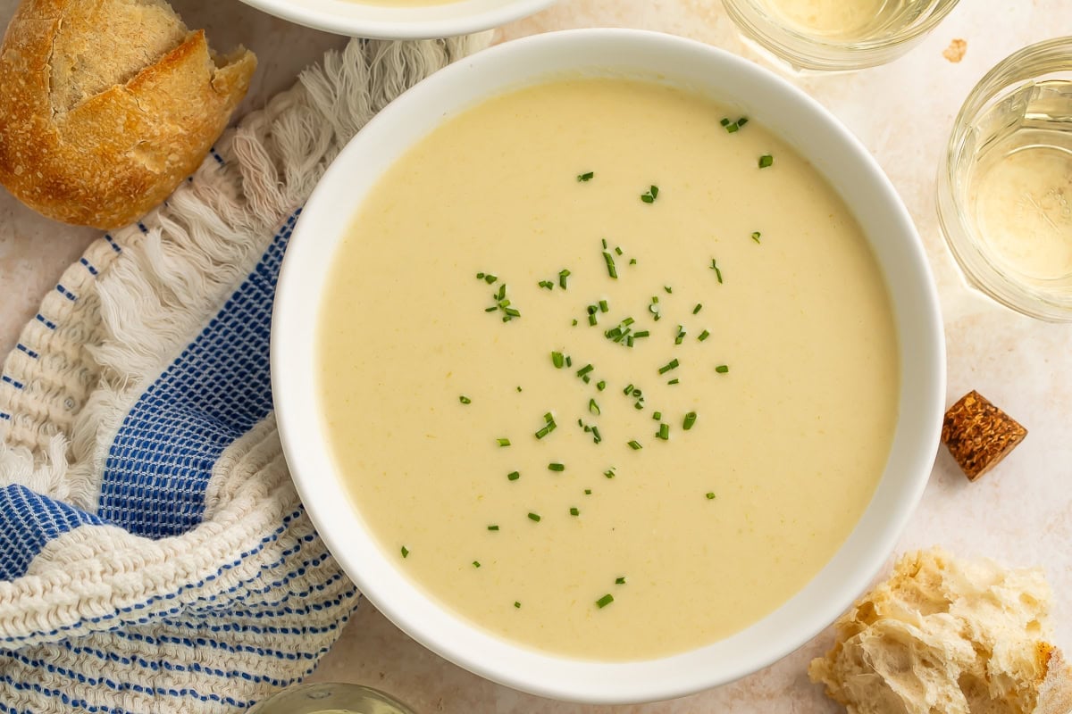 Homemade cream of celery soup in a white bowl, garnished with fresh chives, served with crusty bread and white wine.