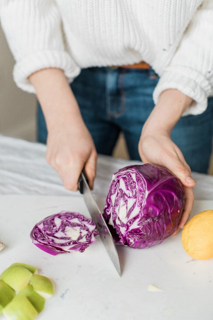 A woman in jeans and a sweater cutting a head of purple cabbage on a kitchen counter