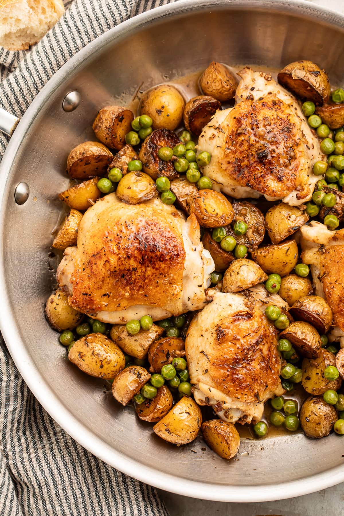 Chicken vesuvio with potatoes and peas in a large silver skillet resting on a striped kitchen towel.
