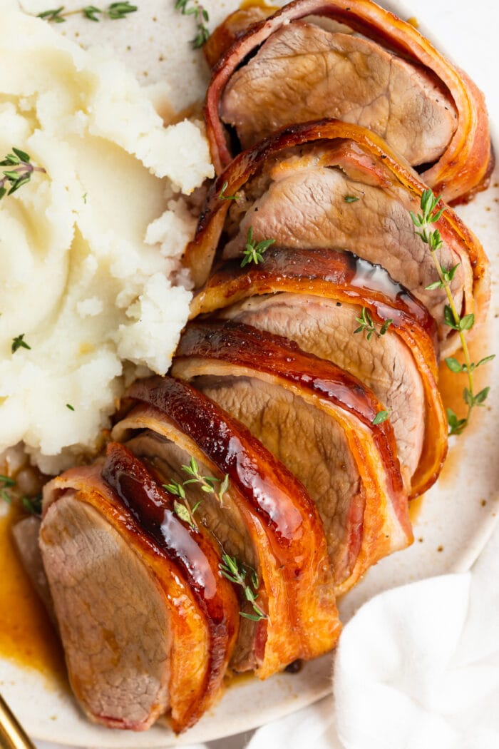 sliced bacon wrapped pork tenderloin on a plate with mashed potatoes on the side