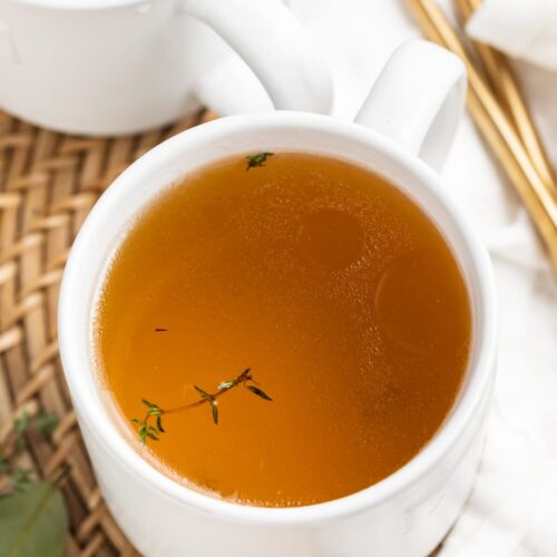 beef consommé in two mugs with fresh thyme on top