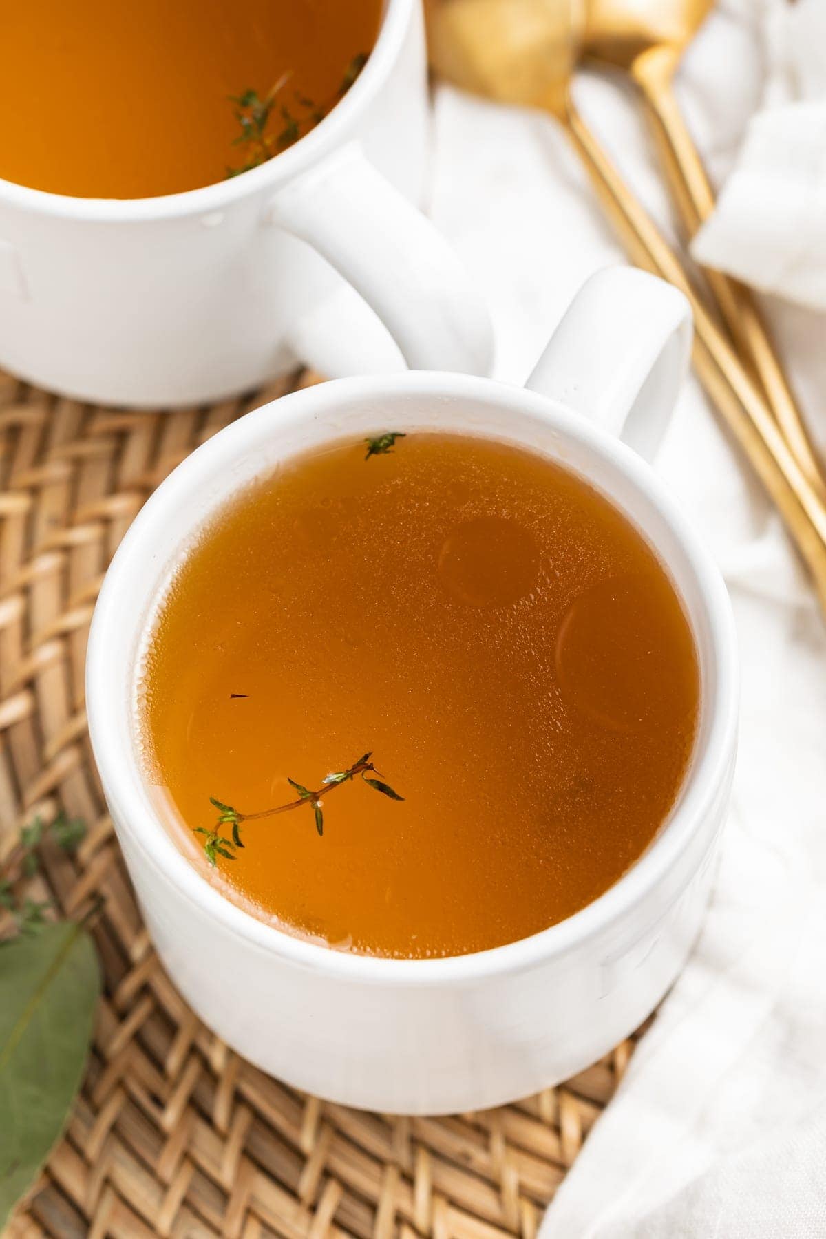 beef consommé in two mugs with fresh thyme on top