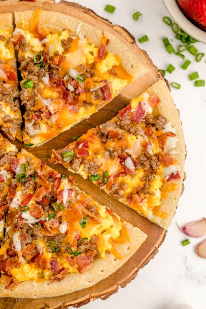 Overhead shot of breakfast pizza cut into slices on a wooden pizza board