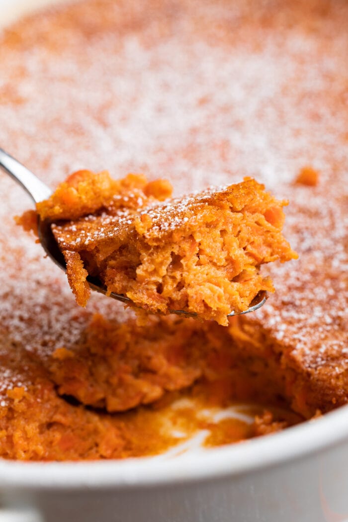 A spoonful of carrot soufflé being lifted out of a casserole dish