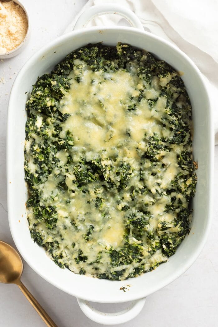 overhead image of spinach casserole in a baking dish with parmesan cheese on the side