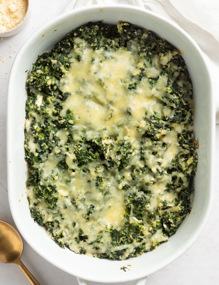 overhead image of spinach casserole in a baking dish with parmesan cheese on the side
