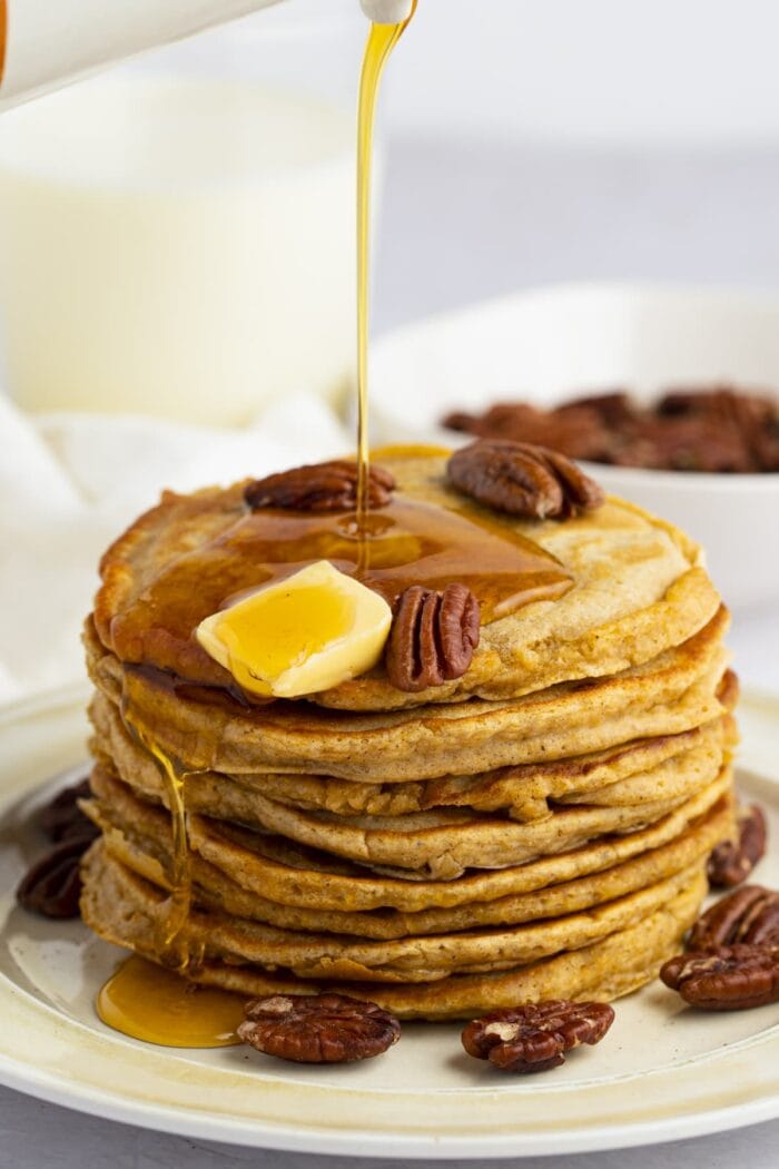 Maple syrup pouring over a stack of sweet potato pancakes topped with pecans and butter