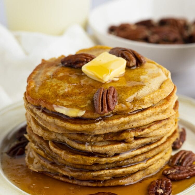 A stack of sweet potato pancakes topped with toasted pecans, butter, and maple syrup