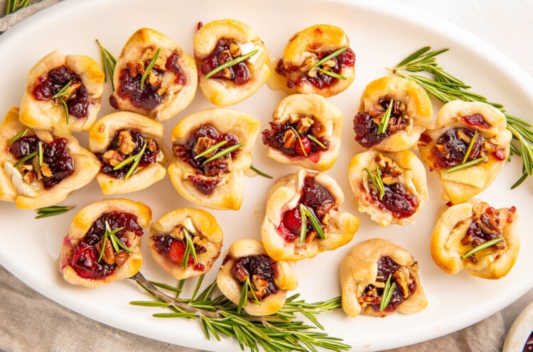 Cranberry brie bites on a serving platter with rosemary sprigs and honey
