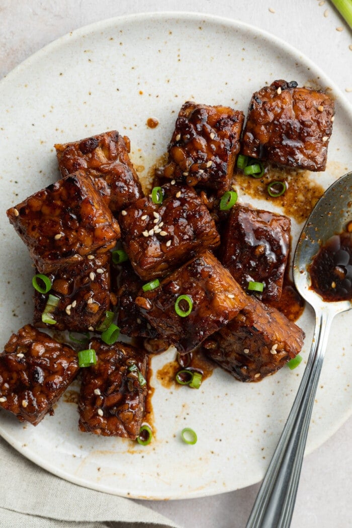 cooked tempeh on a plate with sliced scallions and sesame seeds