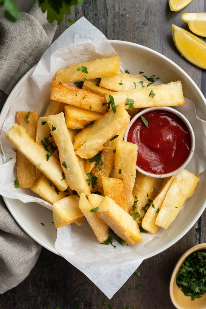 overhead image of yucca fries on a plate with ketchup and fresh parsley on the side
