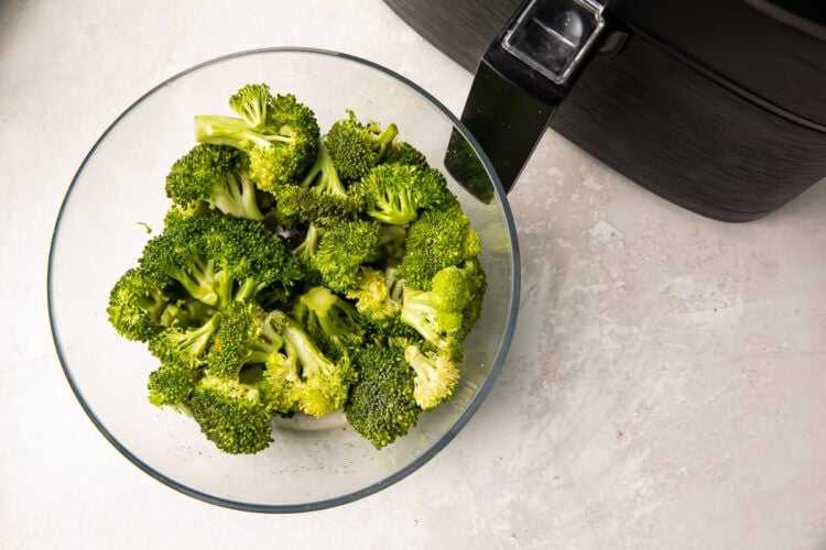 Broccoli in a glass bowl next to an air fryer