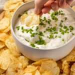 Hand dipping a kettle chip into a bowl of clam dip