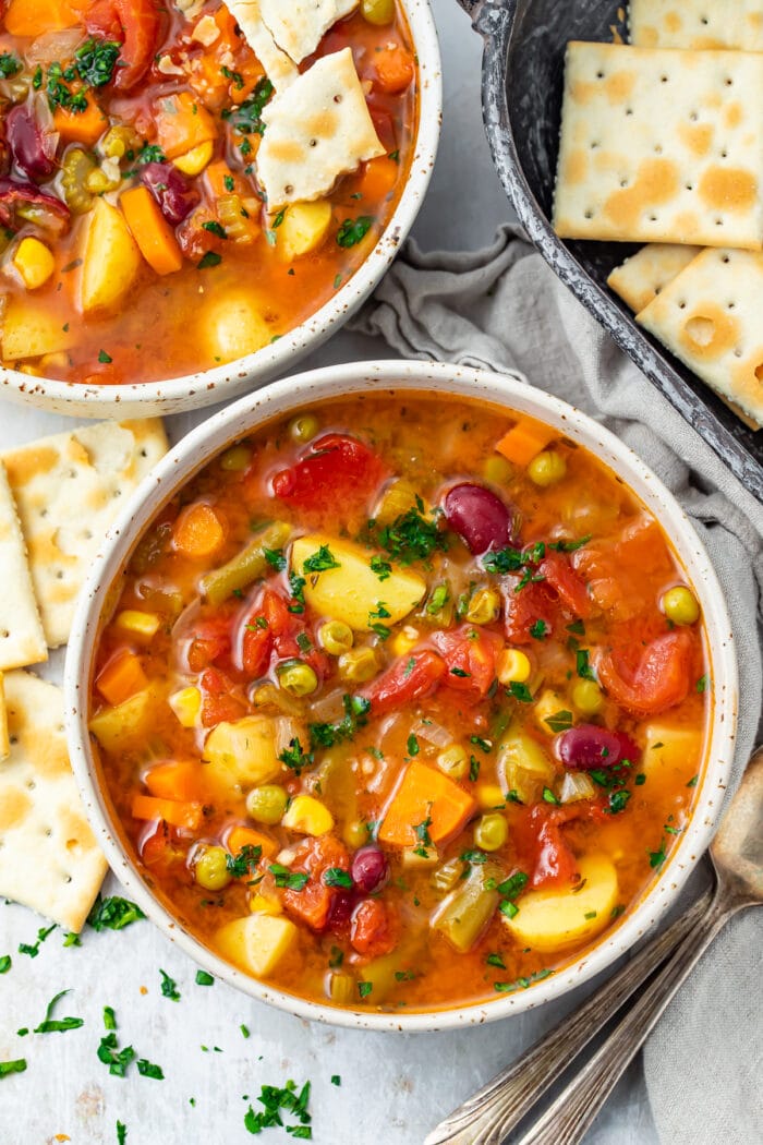 Overhead view of bowls of Instant Pot vegetable soup on a table surrounded by saltine crackers and parsley