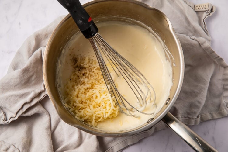 Cheese in milk sauce in saucepan with whisk