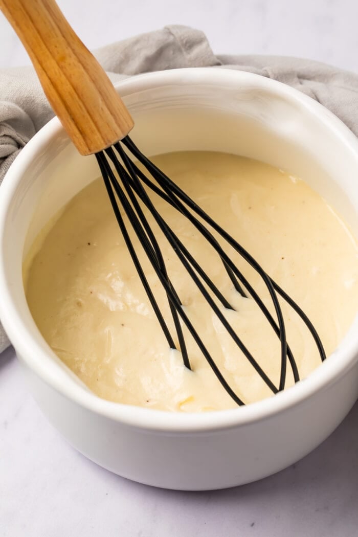 Whisk in a bowl with mornay sauce on a light surface
