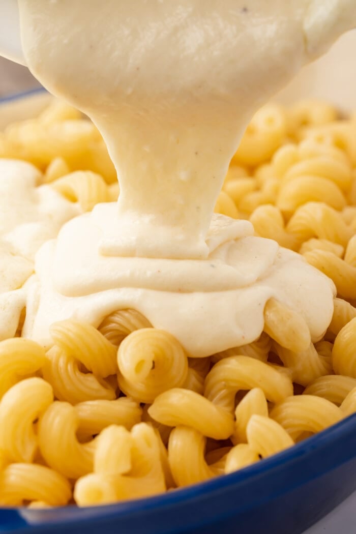 Mornay sauce being poured over a bowl of spiral noodles