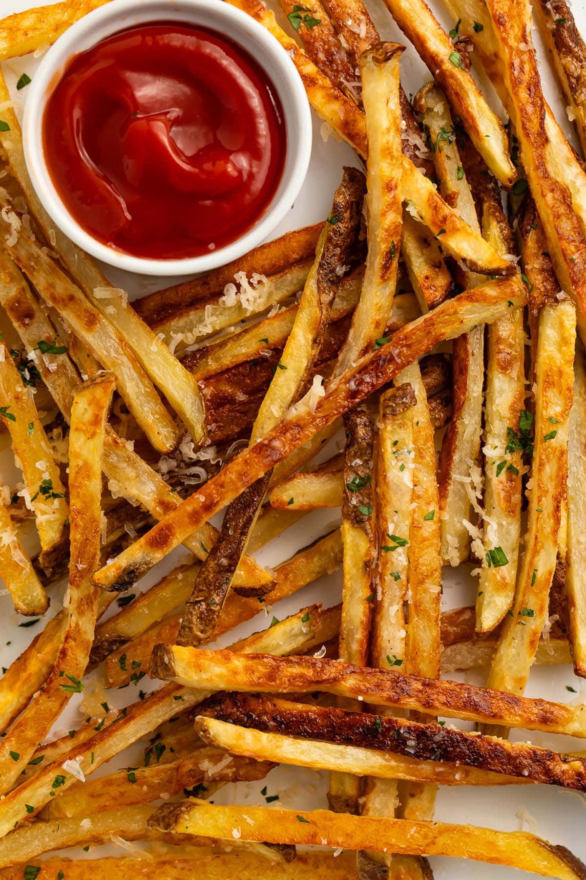 Parmesan truffle fries scattered across a sheet pan lined with parchment paper, next to a ramekin of ketchup.