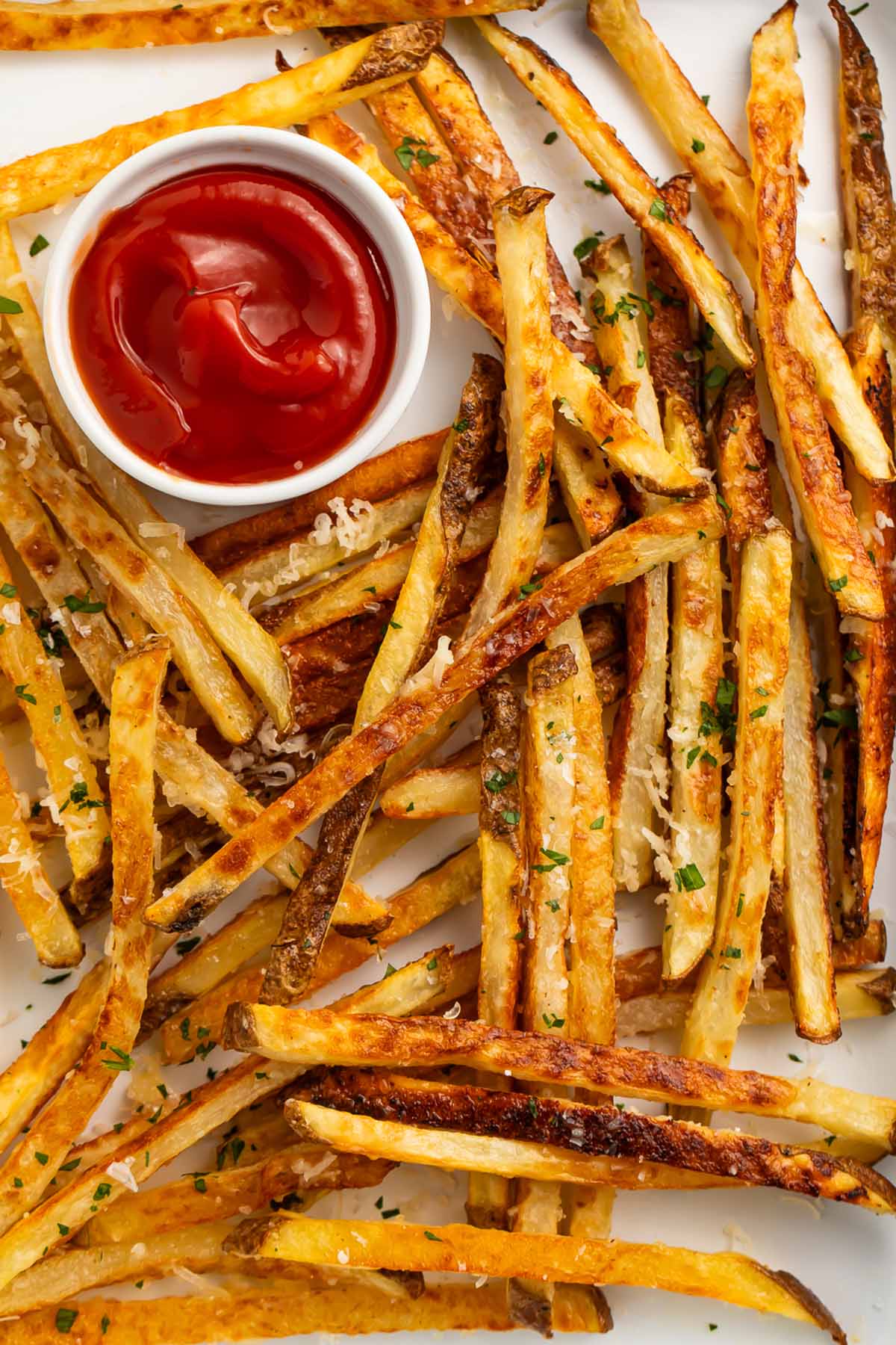 Parmesan truffle fries scattered across a sheet pan lined with parchment paper, next to a ramekin of ketchup.