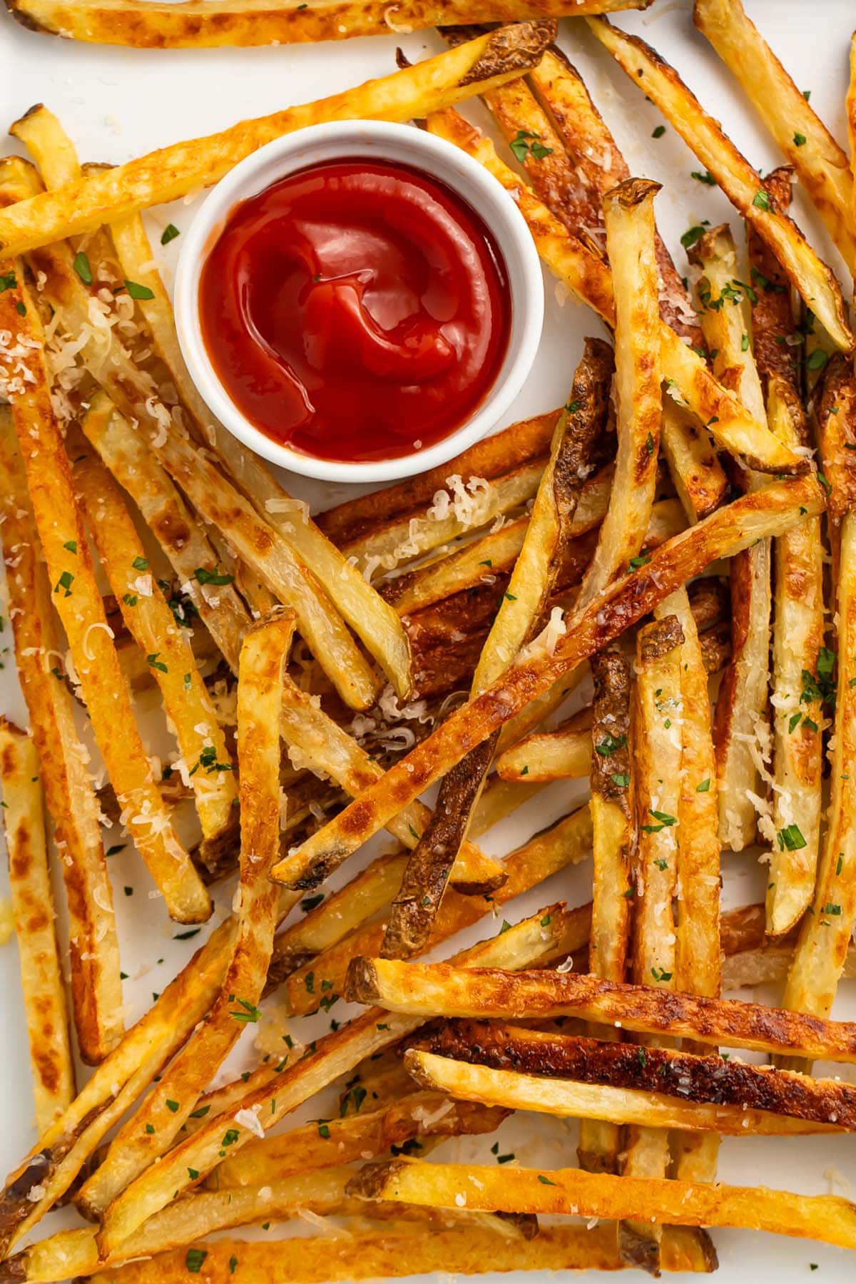 Parmesan truffle fries scattered across a sheet pan lined with parchment paper, next to a ramekin of ketchup.