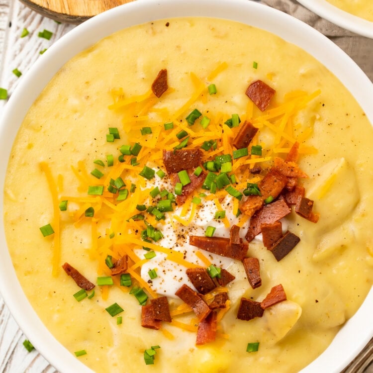 Overhead, close-up view of a bowl of vegan potato soup topped with vegan sour cream and vegan bacon bits