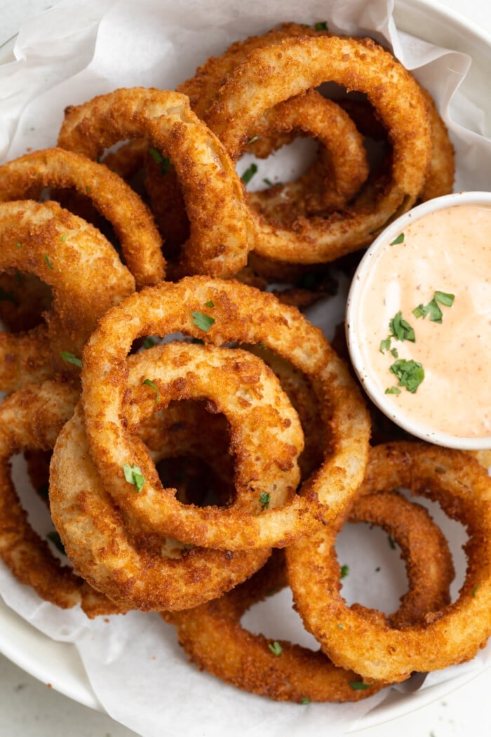 overhead image of frozen onion rings in air fryer in a bowl with bloomin onion sauce on the side