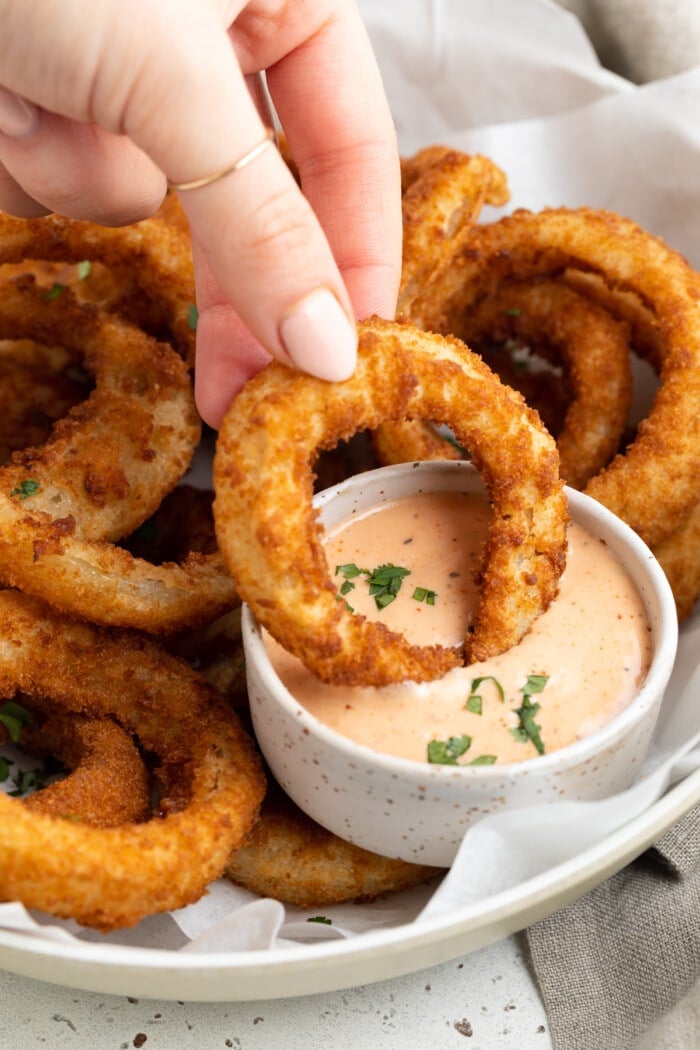 frozen onion ring in air fryer being dipped into bloomin onion sauce