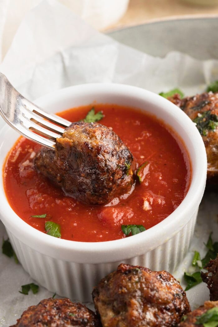 Air fryer meatball on the end of a fork being dipped into a ramekin of marinara sauce
