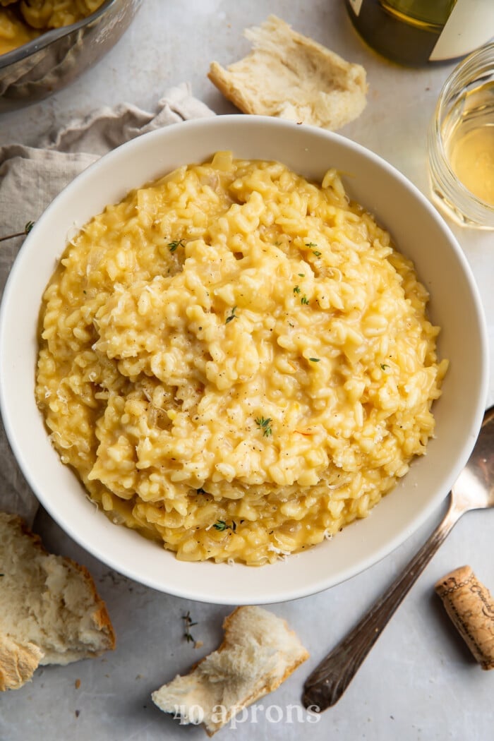 Overhead view of a bowl of risotto on a table surrounded by bread pieces.