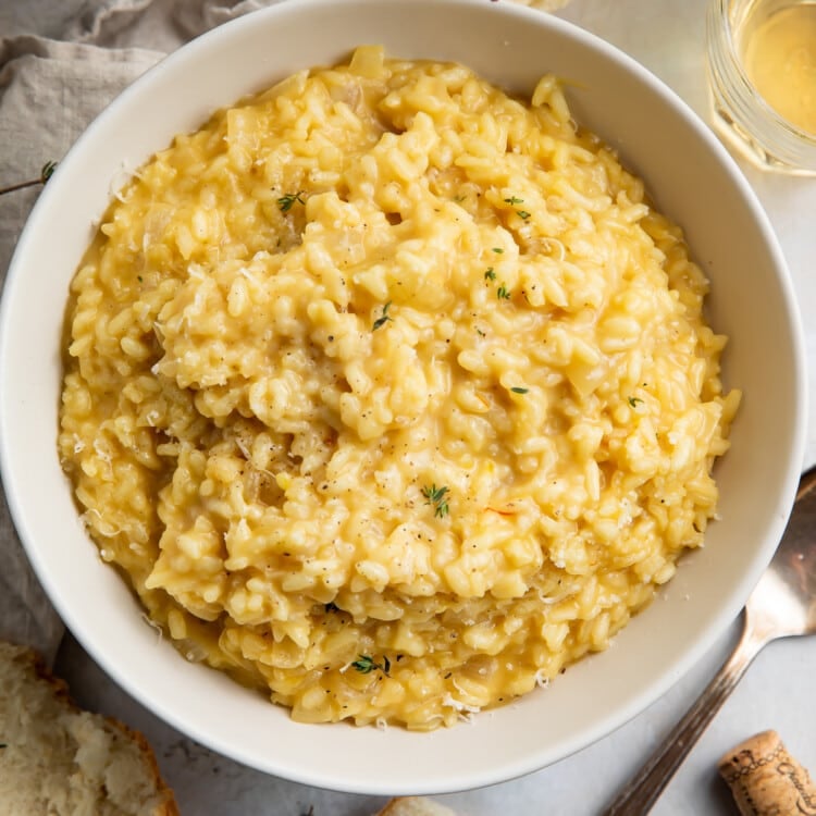 Overhead view of a bowl of risotto on a table surrounded by bread pieces.