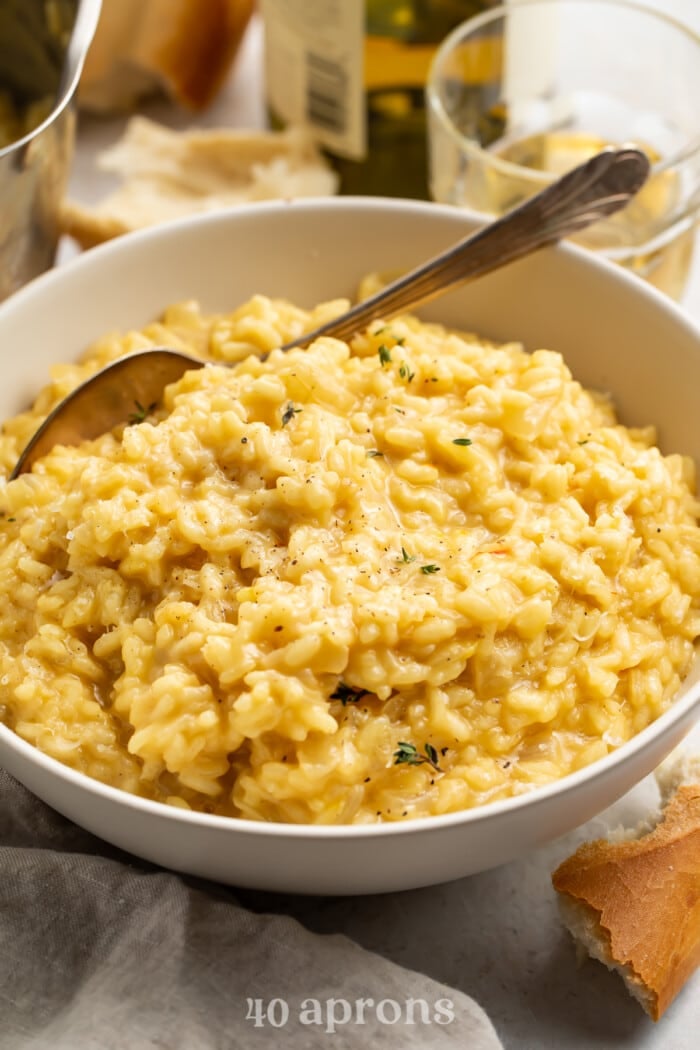Angled view of a large bowl of risotto with a spoon in front of glasses of white wine.