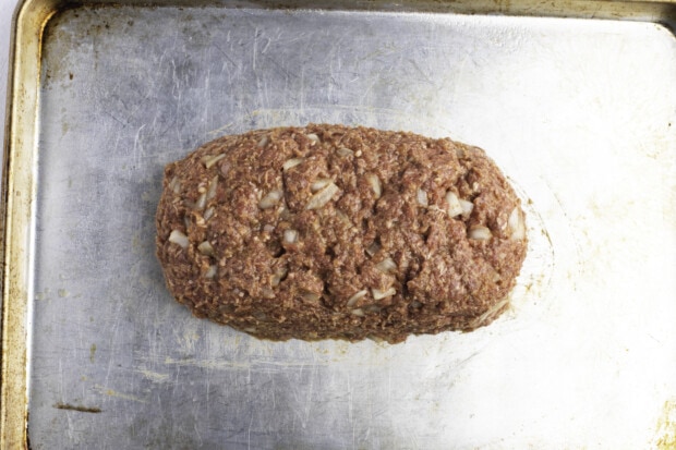 Loaf-shaped, uncooked meatloaf on baking sheet