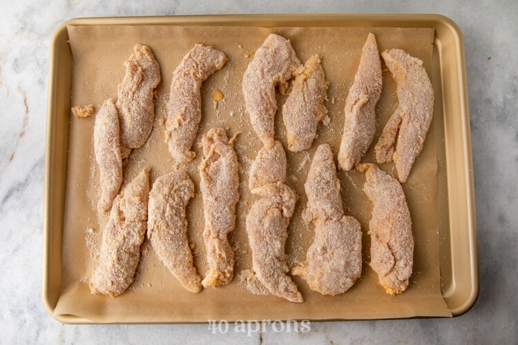Chicken tenders breaded on baking sheet lined with parchment paper