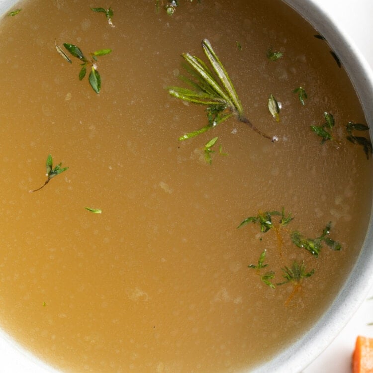 close-up overhead image of bone broth in a bowl with fresh herbs on top
