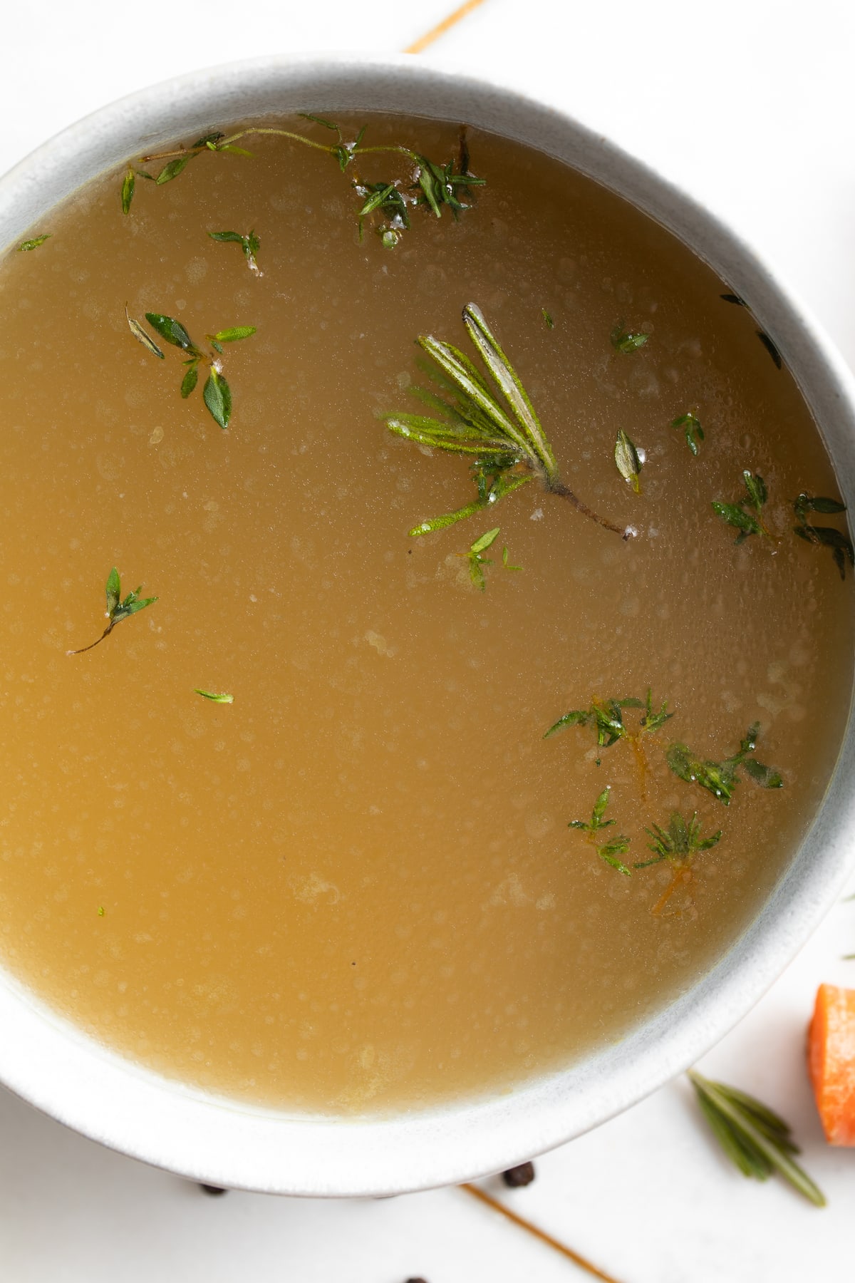 close-up overhead image of bone broth in a bowl with fresh herbs on top