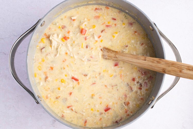 Overhead view of chicken corn chowder in a large, heavy-bottomed pot with wooden spoon on a white background.
