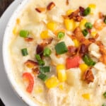 Overhead view of a bowl of chicken corn chowder with tomato and bacon on a wooden table.