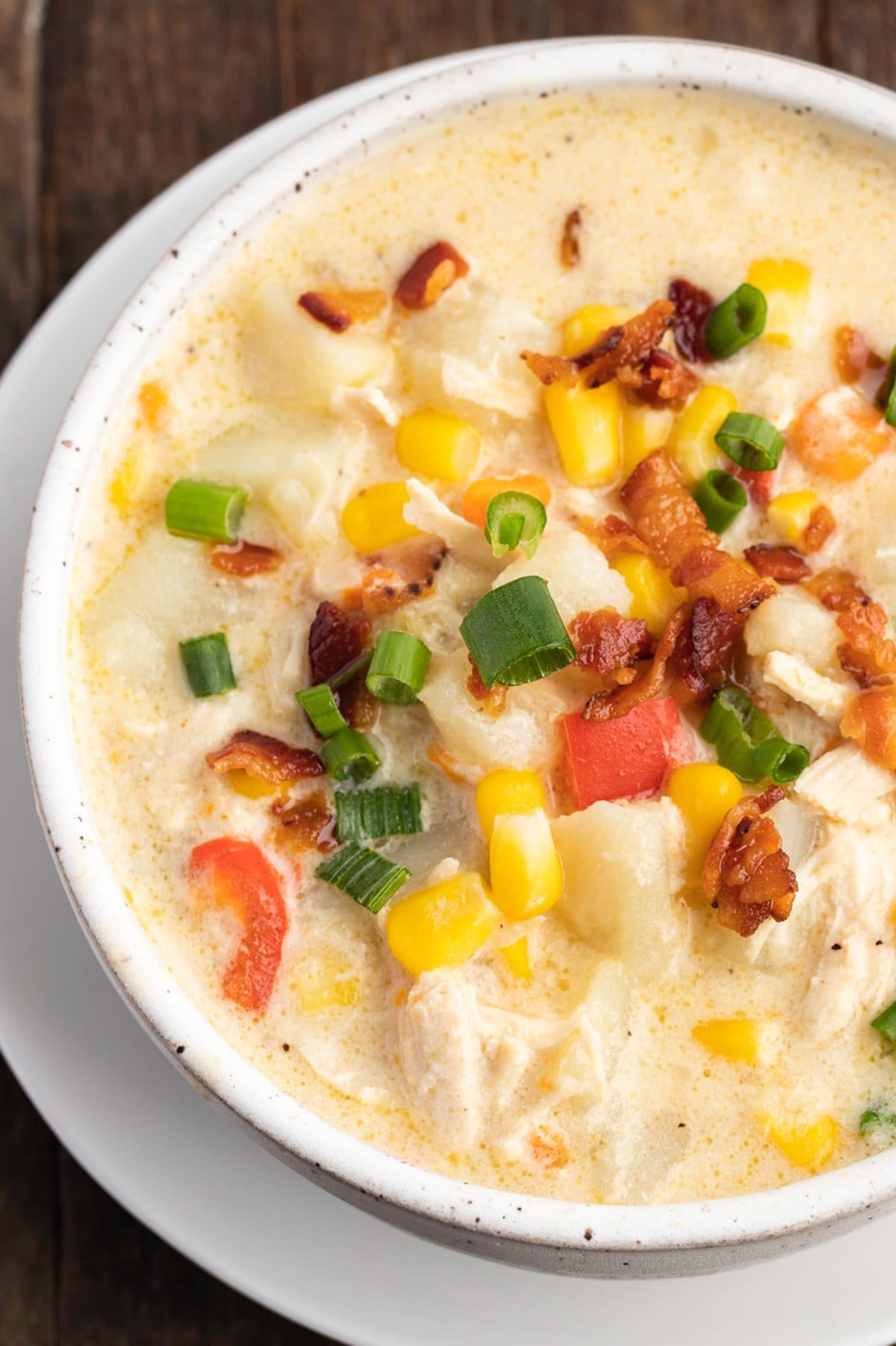 Overhead view of a bowl of chicken corn chowder with tomato and bacon on a wooden table.