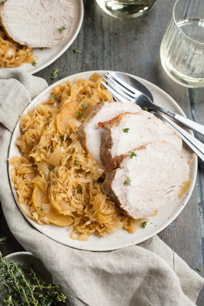 sauerkraut and sliced pork roast on a plate with white wine on the side