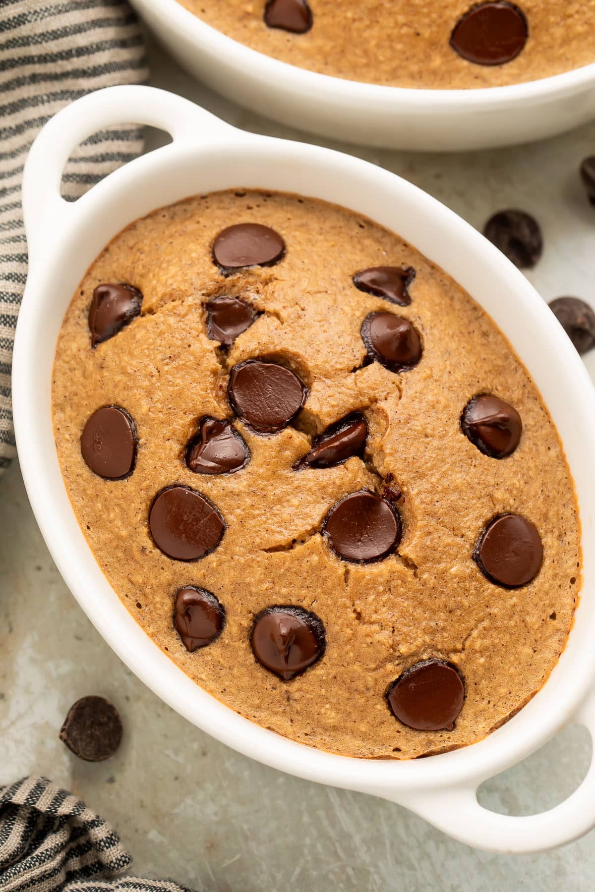 Top-down, close-up view of an oblong single-serve ramekin holding fluffy blended baked oats dotted with chocolate chips.