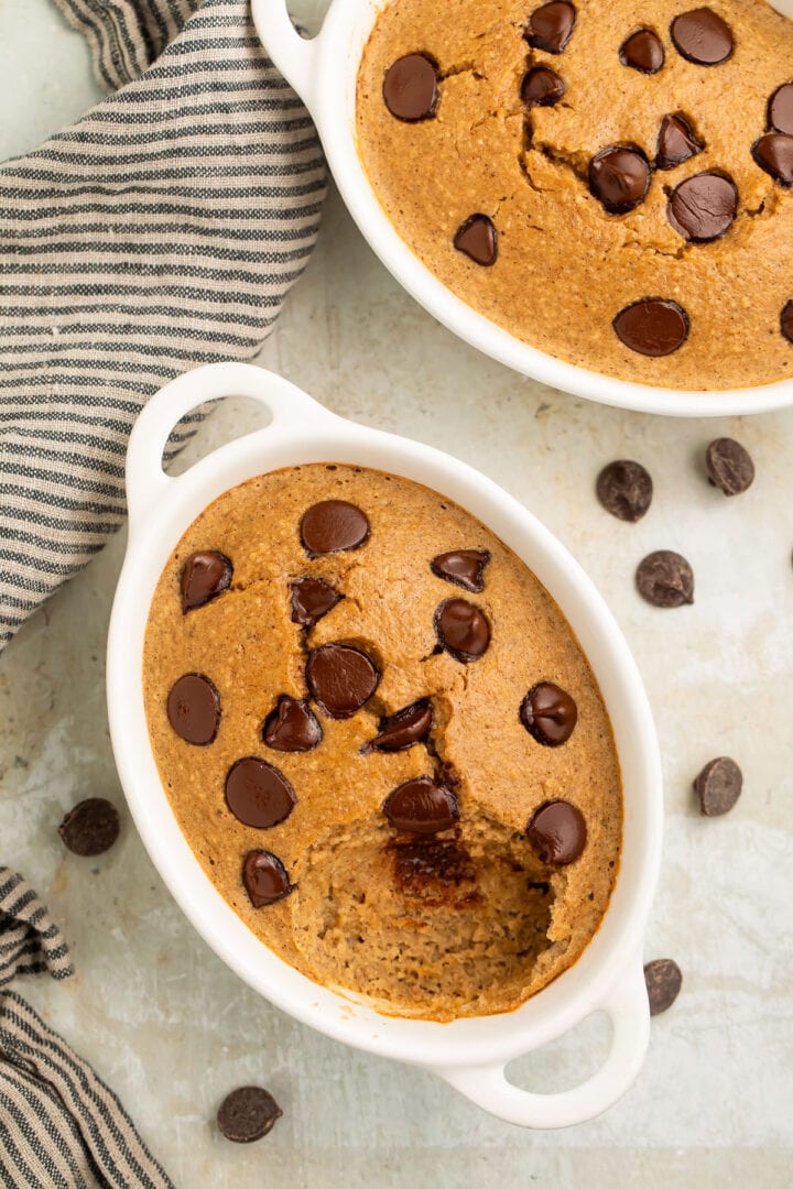 Top-down, overhead view of two oblong single-serve ramekins holding fluffy blended baked oats dotted with chocolate chips.