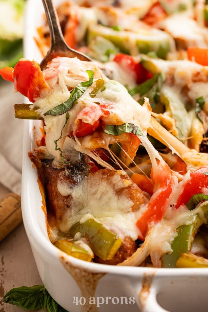 A spoonful of cheesy Italian sausage and bell pepper casserole being lifted out of a casserole dish.