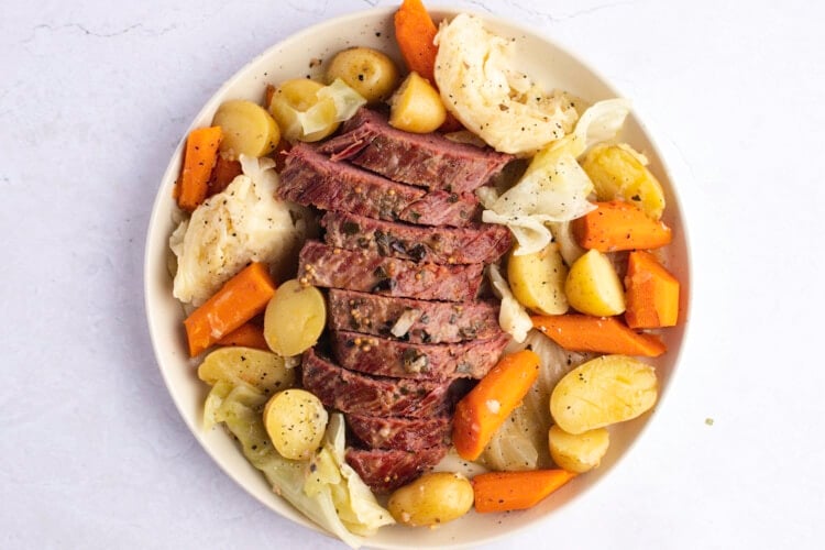 Sliced corned beef brisket with potatoes, carrots, and cabbage on white platter.