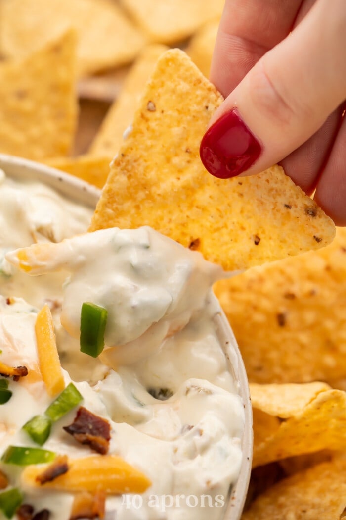 A tortilla chip being dipped into the bowl of jalapeno popper dip.