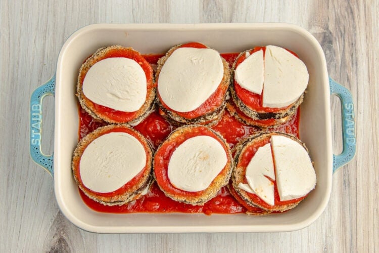 Unbaked keto eggplant parmesan topped with discs of mozzarella in a 9x13 baking dish.